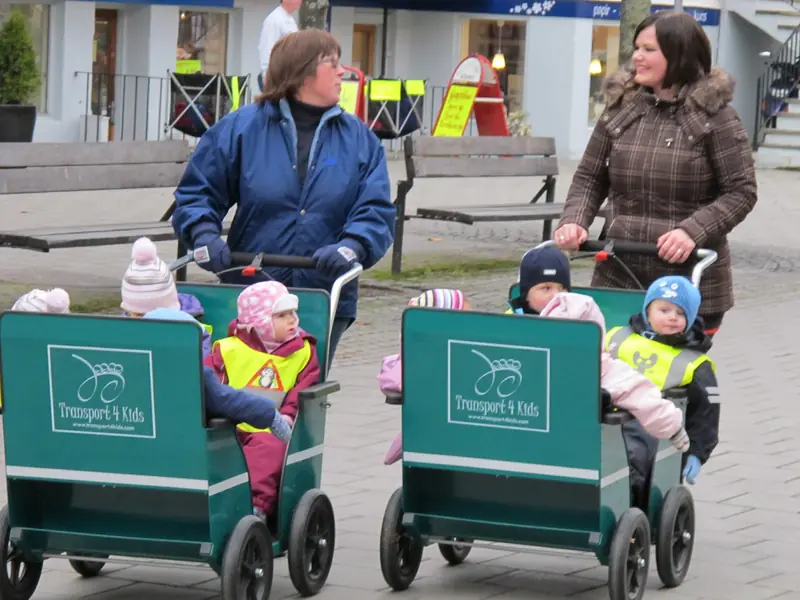 To barnehageansatte triller hver sin Englebarnekspressen med småbarn over et torg.